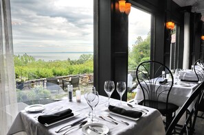 A dining table set with white tablecloth, plates, cutlery, and wine glasses, overlooking a scenic view of greenery and water. - Auberge des Falaises (La Malbaie)