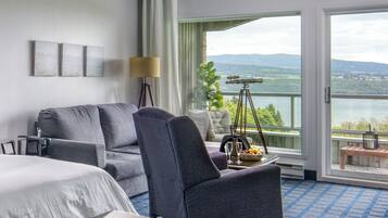 Habitación de hotel con cama, sofá, escritorio, lámpara, un telescopio y vistas a un lago y montañas.