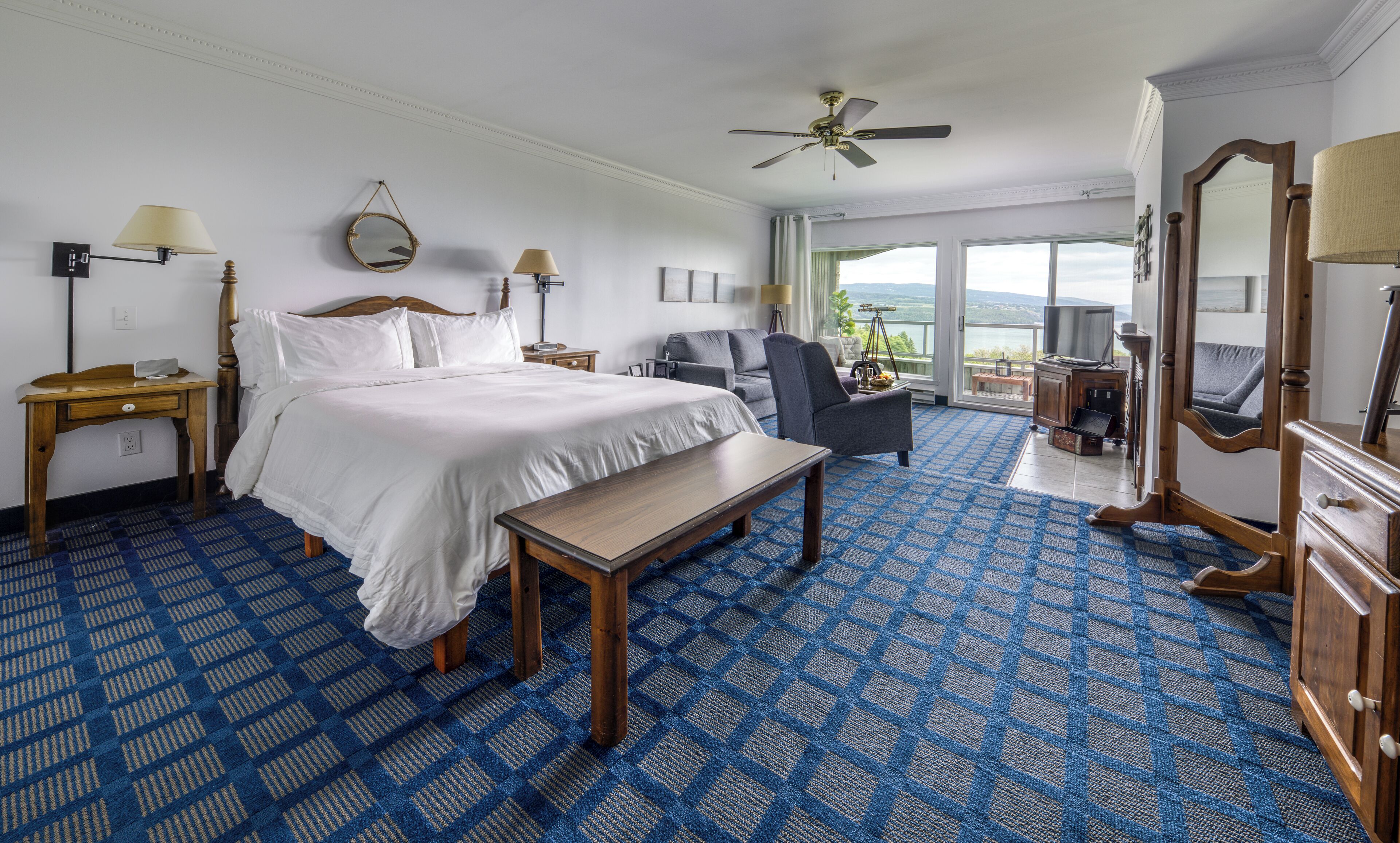 Habitación de hotel con una cama grande, un escritorio, una silla, un ventilador de techo y vistas al exterior.
