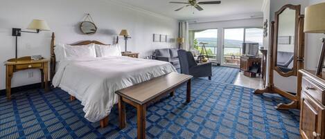 A hotel room with a large bed, a desk, a chair, a ceiling fan, and a view of the outdoors.