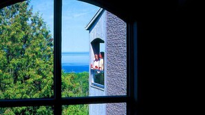 Une vue à travers la fenêtre d’un bâtiment à la façade en pierre, doté d’un balcon.