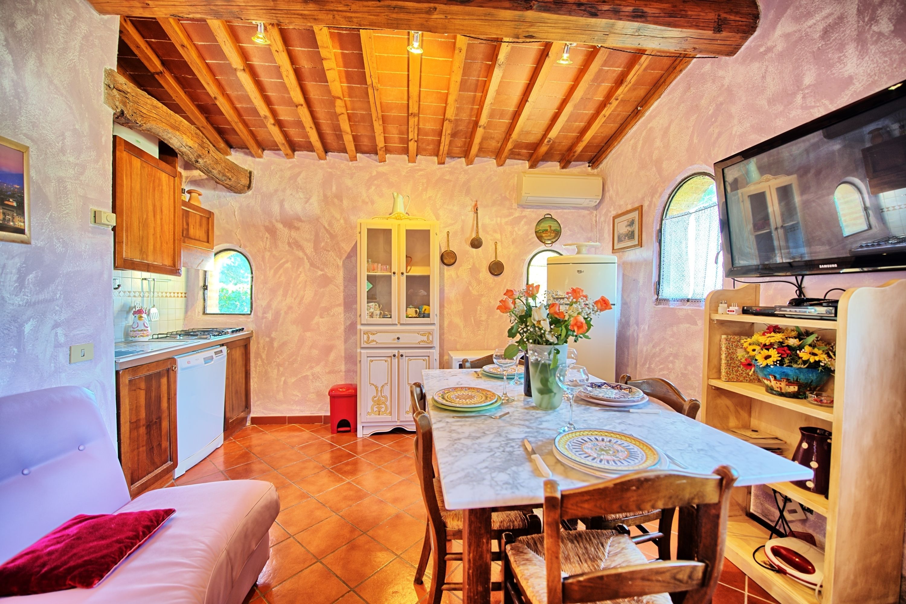 A cozy kitchen with wooden cabinets, a dining table set for two, and a television on the right.