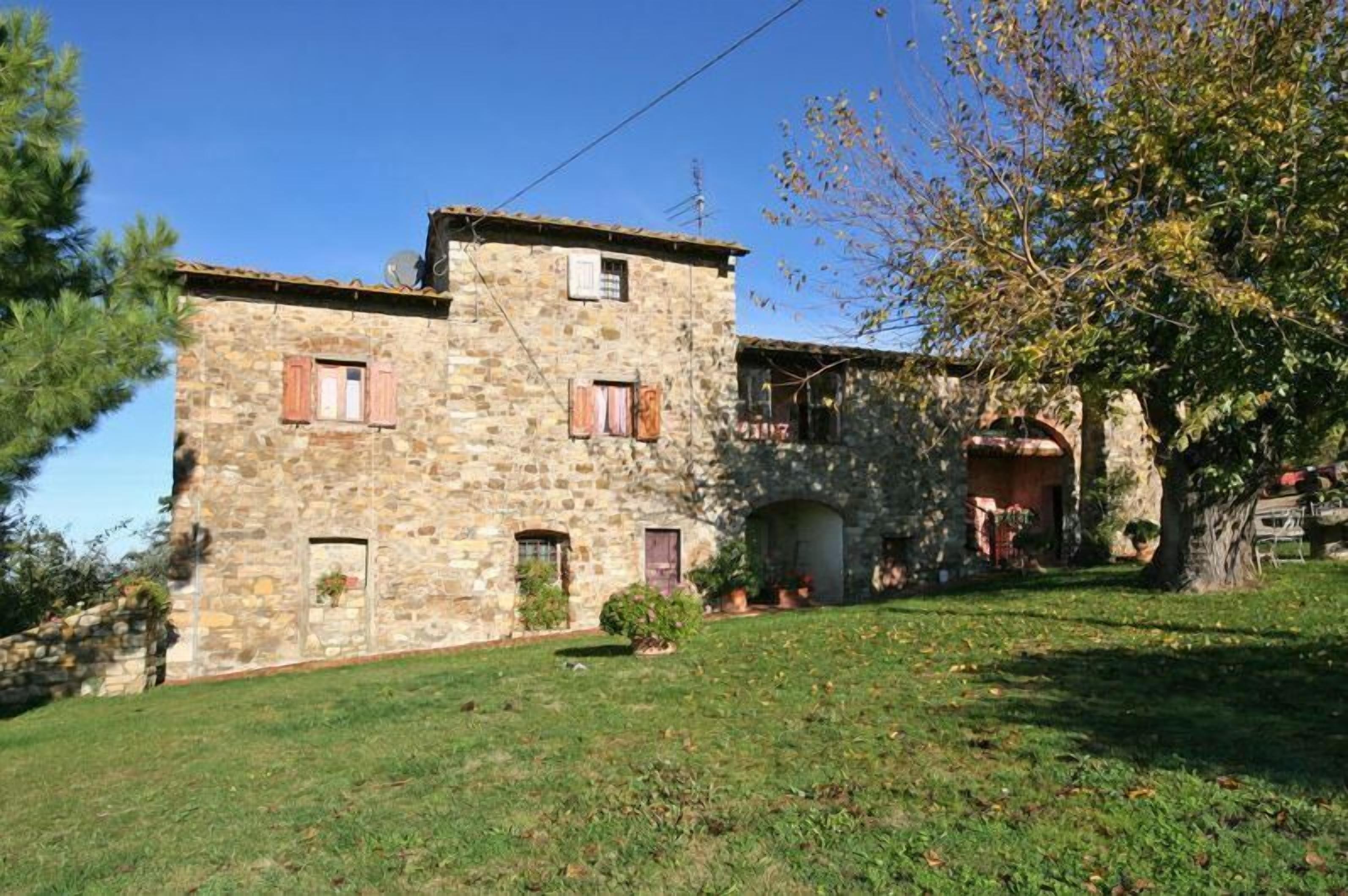 A stone building with a sloped roof, multiple windows, and a small garden area with trees and shrubs.