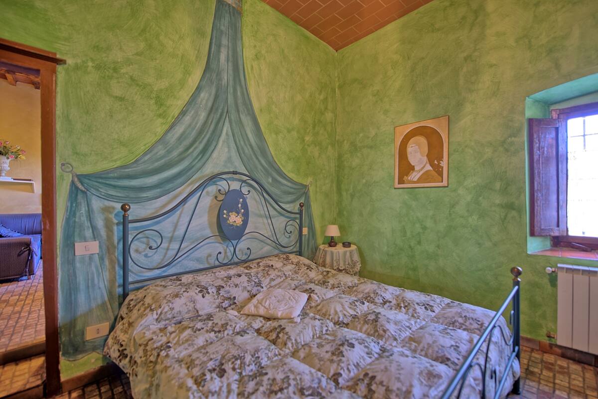 Ein Schlafzimmer mit Himmelsbett, einem kleinen Nachttisch mit Lampe und einem gerahmten Bild an der Wand.