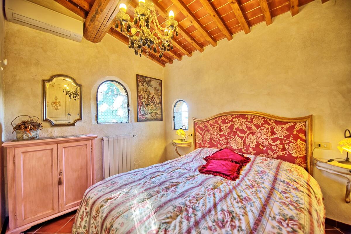 Ein Schlafzimmer mit Holzboden, einem Bett mit floralem Überwurf, einem rosa Schrank und zwei Wandleuchten.