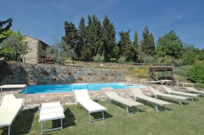 A swimming pool with lounge chairs, a stone wall, and a wooden pergola. - Casa Anna (Barberino Tavarnelle)