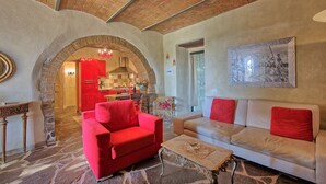 A living room with a red sofa, a beige sofa, and a stone floor. There is a kitchen in the background with red accents. - Casa Anna (Barberino Tavarnelle)