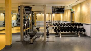 A gym with weightlifting equipment, mirrors, and a wall-mounted rack of dumbbells.