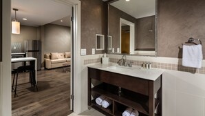 A modern bathroom with a large mirror, a sink, and a vanity. There is a wooden floor and a beige sofa in the adjacent living area. - Aventura Hotel (Los Angeles)