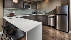 A modern kitchen with a white marble island, dark wooden cabinets, stainless steel appliances, and a tiled backsplash. - Aventura Hotel (Los Angeles)