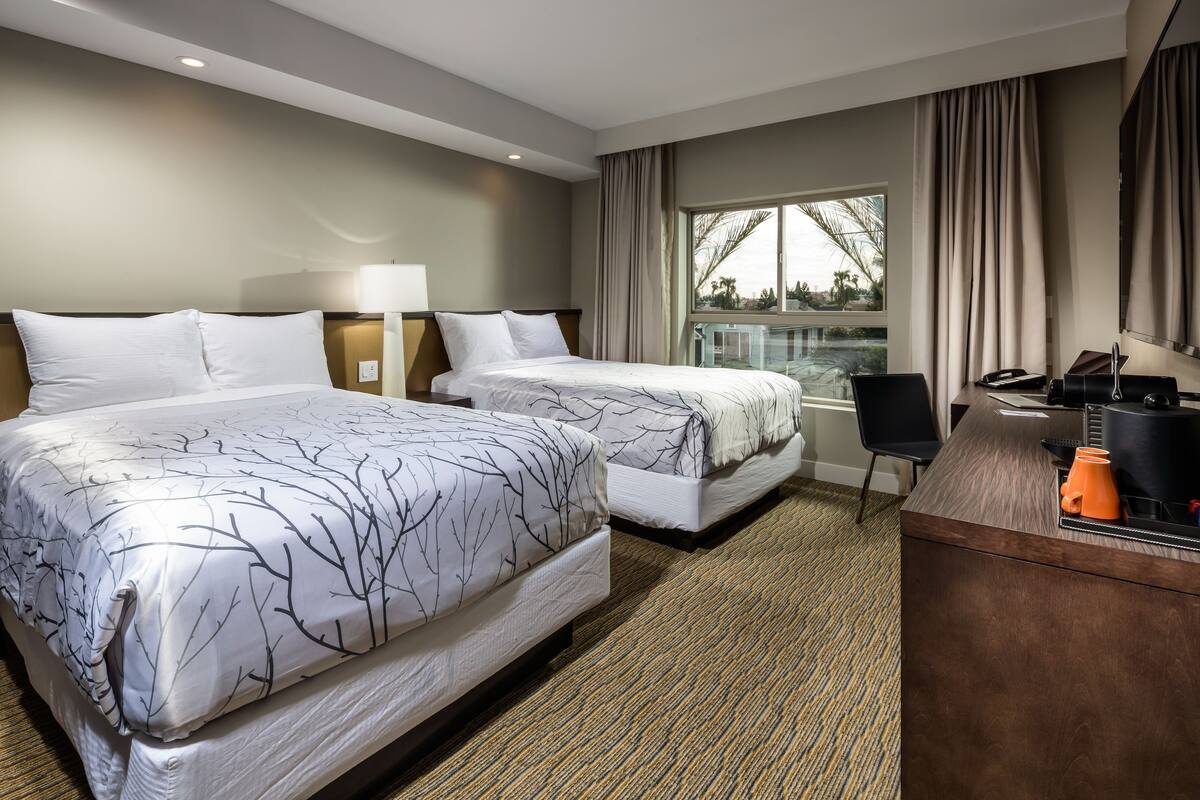 A hotel room with two beds, a desk, and a window with curtains.