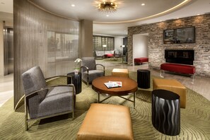 A modern living room with a sofa, armchair, coffee table, and ottoman. There is a fireplace and a television mounted on the wall.