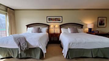 A hotel room with two beds, each with a green skirted base, a headboard, and a white quilted bedspread. There is a window with curtains, a framed picture on the wall, and a nightstand with a lamp.