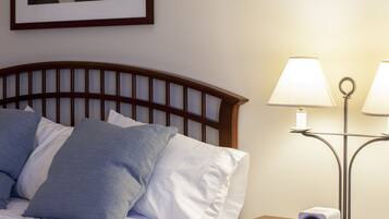 A neatly made bed with pillows, a bedside table with a lamp, a clock, and a framed picture on the wall.