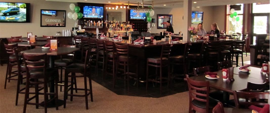 A bar area with multiple seating arrangements, a bar counter, and televisions displaying sports.