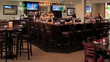 A bar area with multiple seating arrangements, a bar counter, and televisions displaying sports.