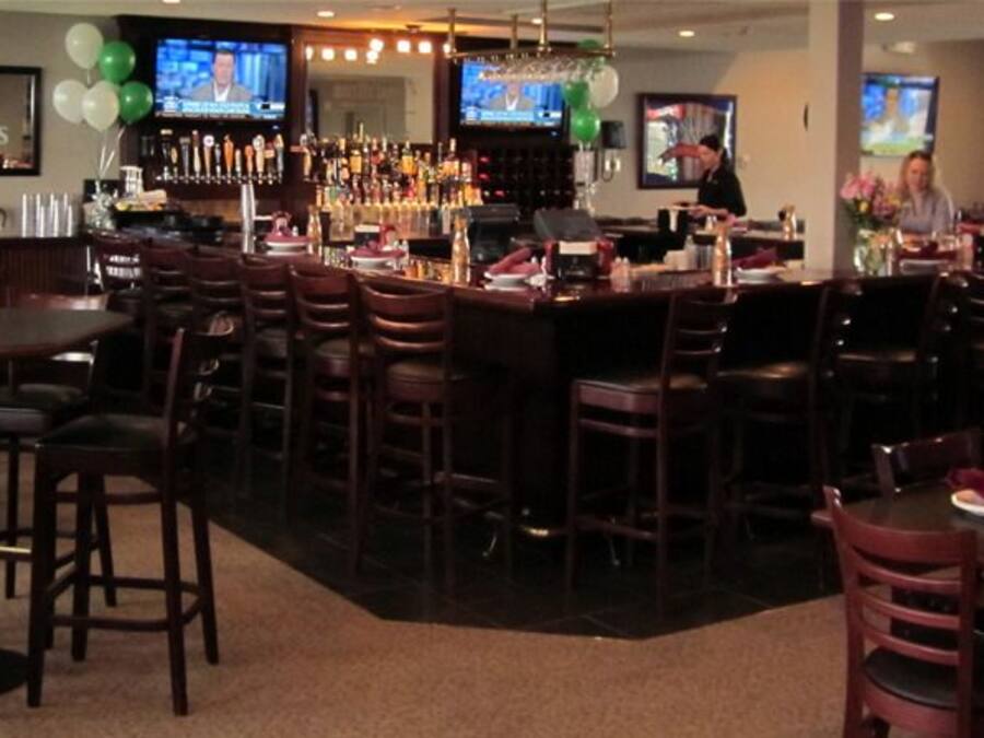 A bar area with multiple seating arrangements, a bar counter, and televisions displaying sports.