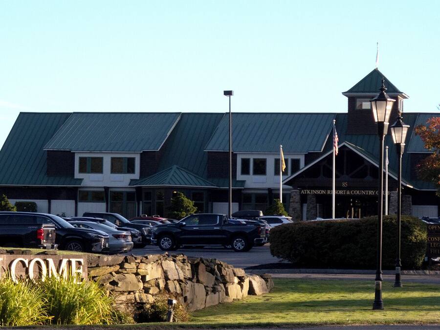 A hotel entrance with a 'WELCOME' sign, a parking lot, and a building with a green roof.