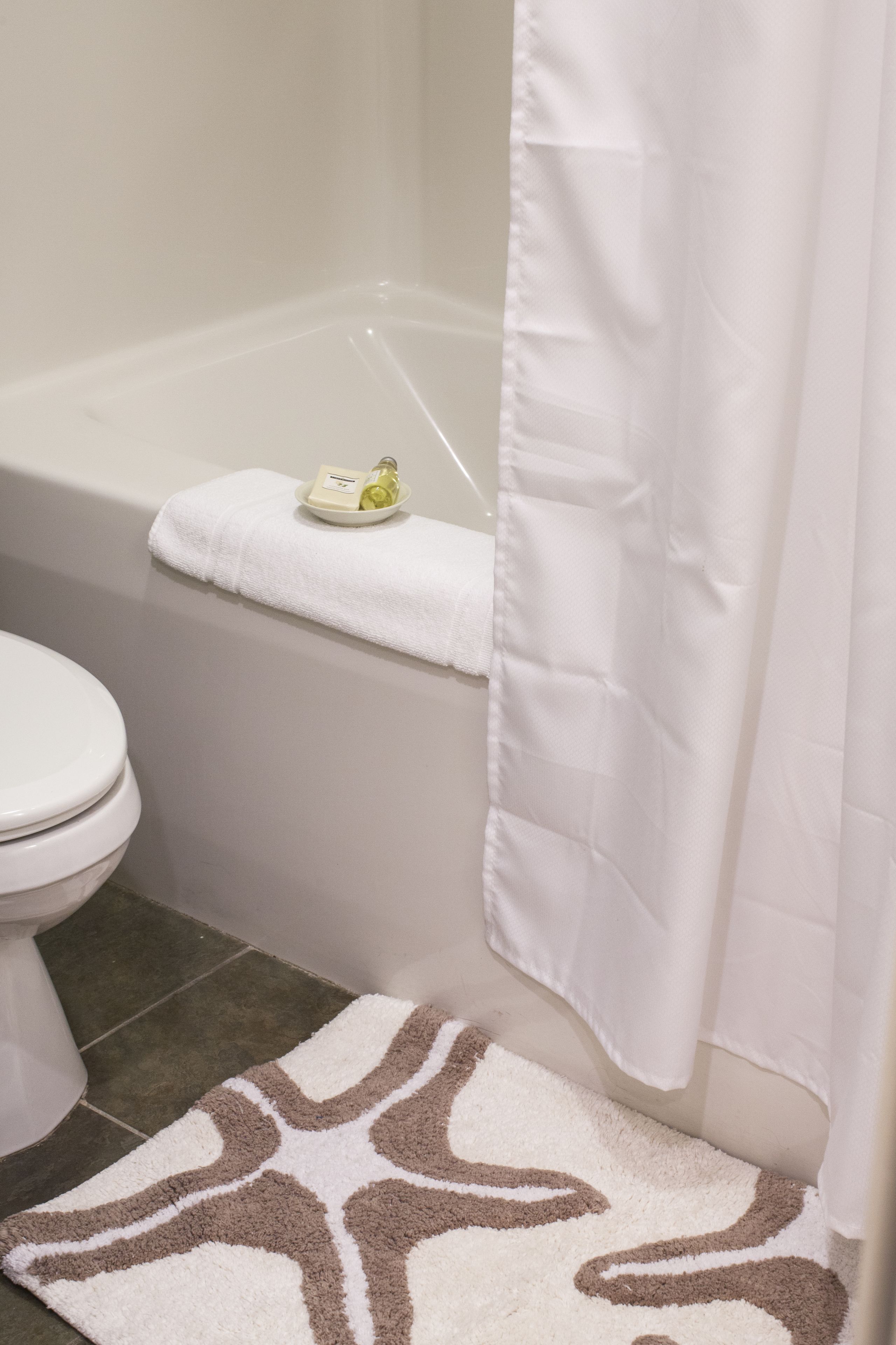 A bathroom with a white toilet, a bathtub with a white towel on the edge, and a patterned rug on the floor.