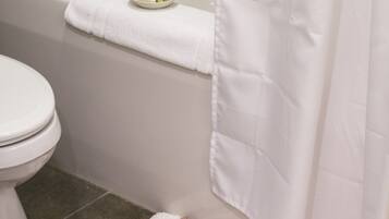 A bathroom with a white toilet, a bathtub with a white towel on the edge, and a patterned rug on the floor.