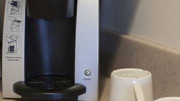 Eine Keurig-Kaffeemaschine auf einer Küchenarbeitsplatte, zusammen mit zwei weißen Tassen und einem Kartenspiel mit floralem Muster.