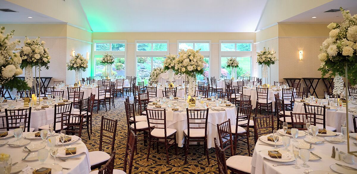 Un salón de banquetes con mesas redondas, manteles blancos y centros de mesa florales.
