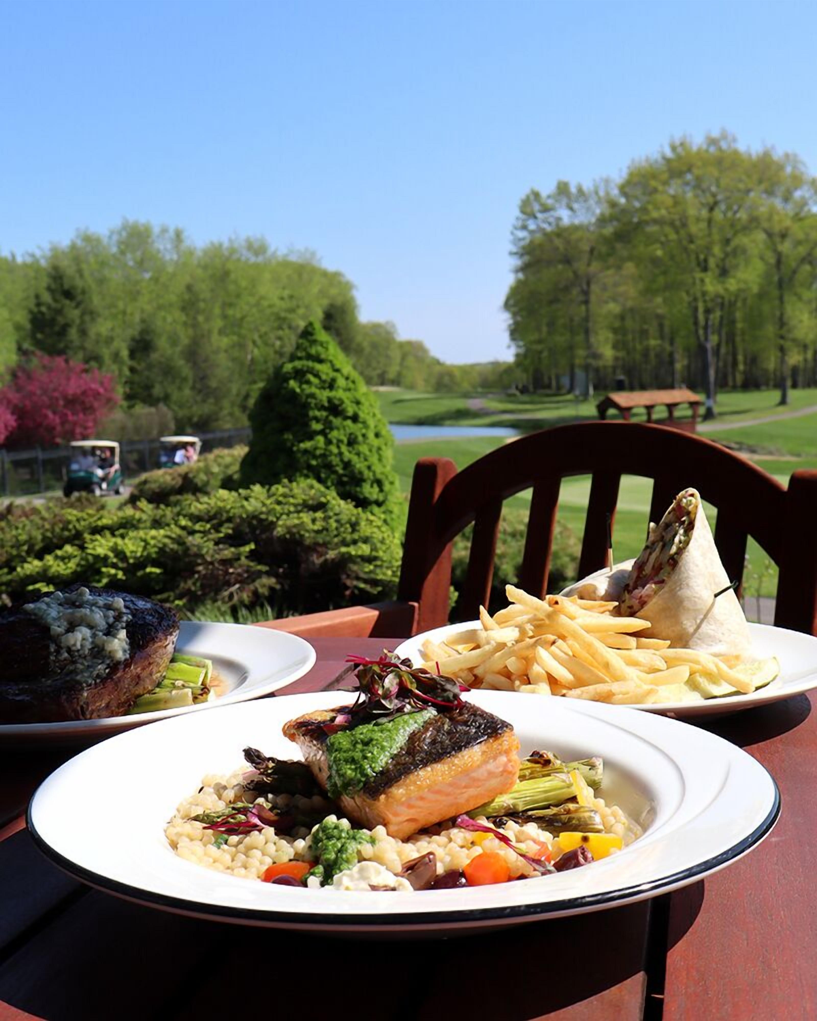 A dining table with plates of food, a golf course in the background, and a picnic table.