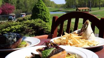 A dining table with plates of food, a golf course in the background, and a picnic table.