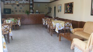 A dining area with tables and chairs, a kitchen area with a counter, and a sofa. - Varelis (Rhodes)