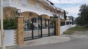 A multi-story residential building with a gated entrance, a balcony on the upper floor, and a stone wall surrounding the property. - Varelis (Rhodes)