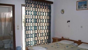 A bedroom with a wooden bed, a patterned curtain, a small bedside table, and a wall-mounted light. - Varelis (Rhodes)