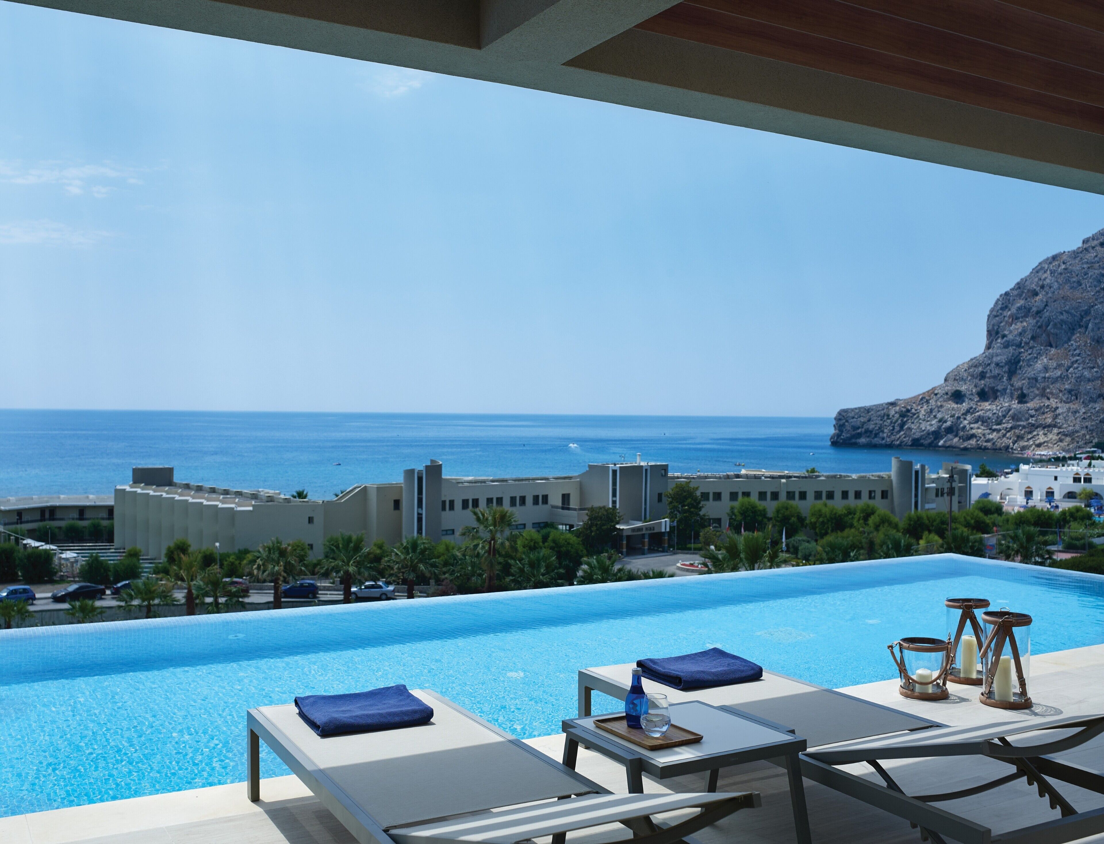 Ein Poolbereich mit Liegestühlen, einem Tisch und einem Handtuch, mit Blick auf das Meer und Gebäude.