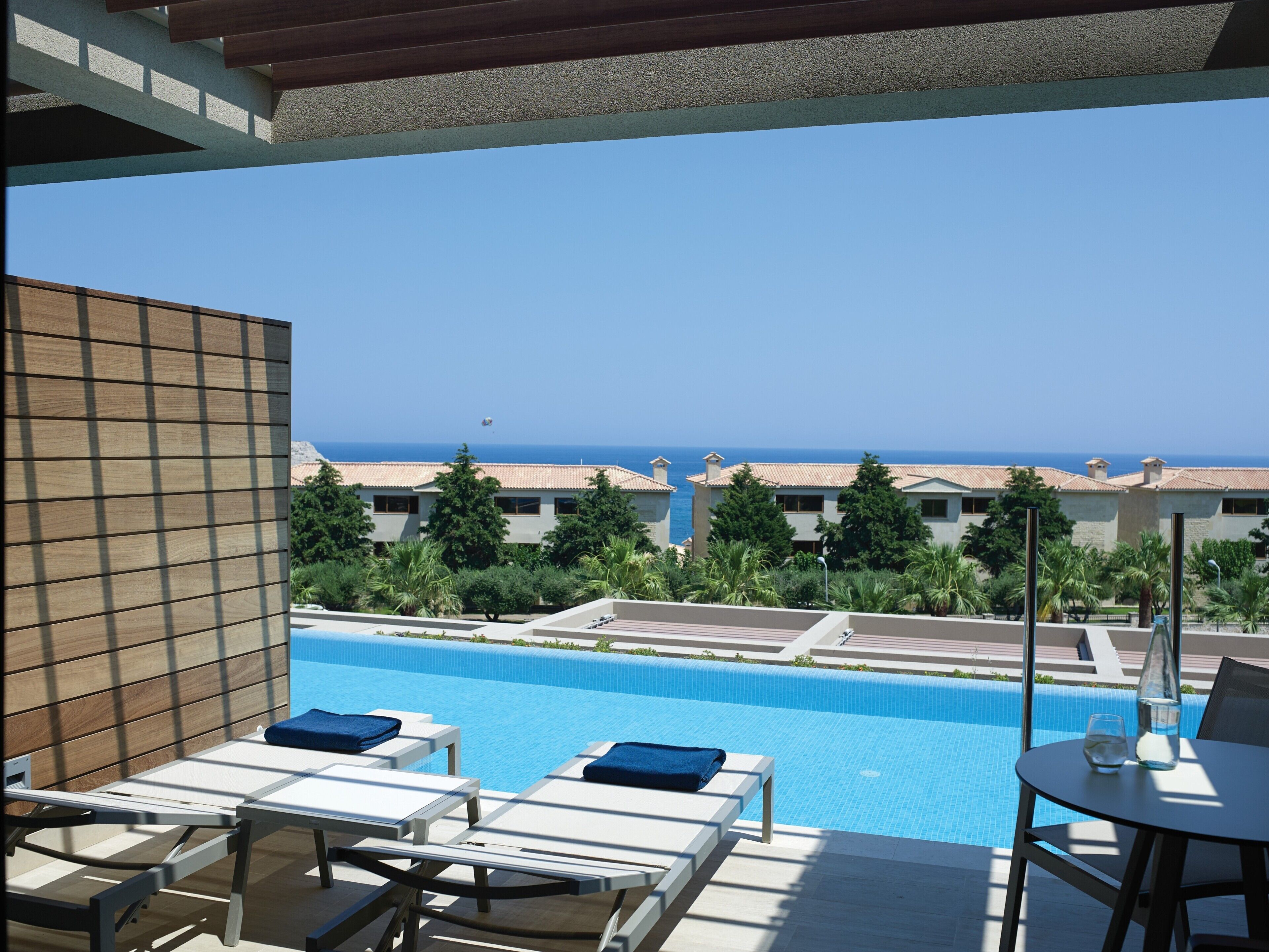 A poolside area with lounge chairs and a table, overlooking a clear blue sky and a distant view of the sea.