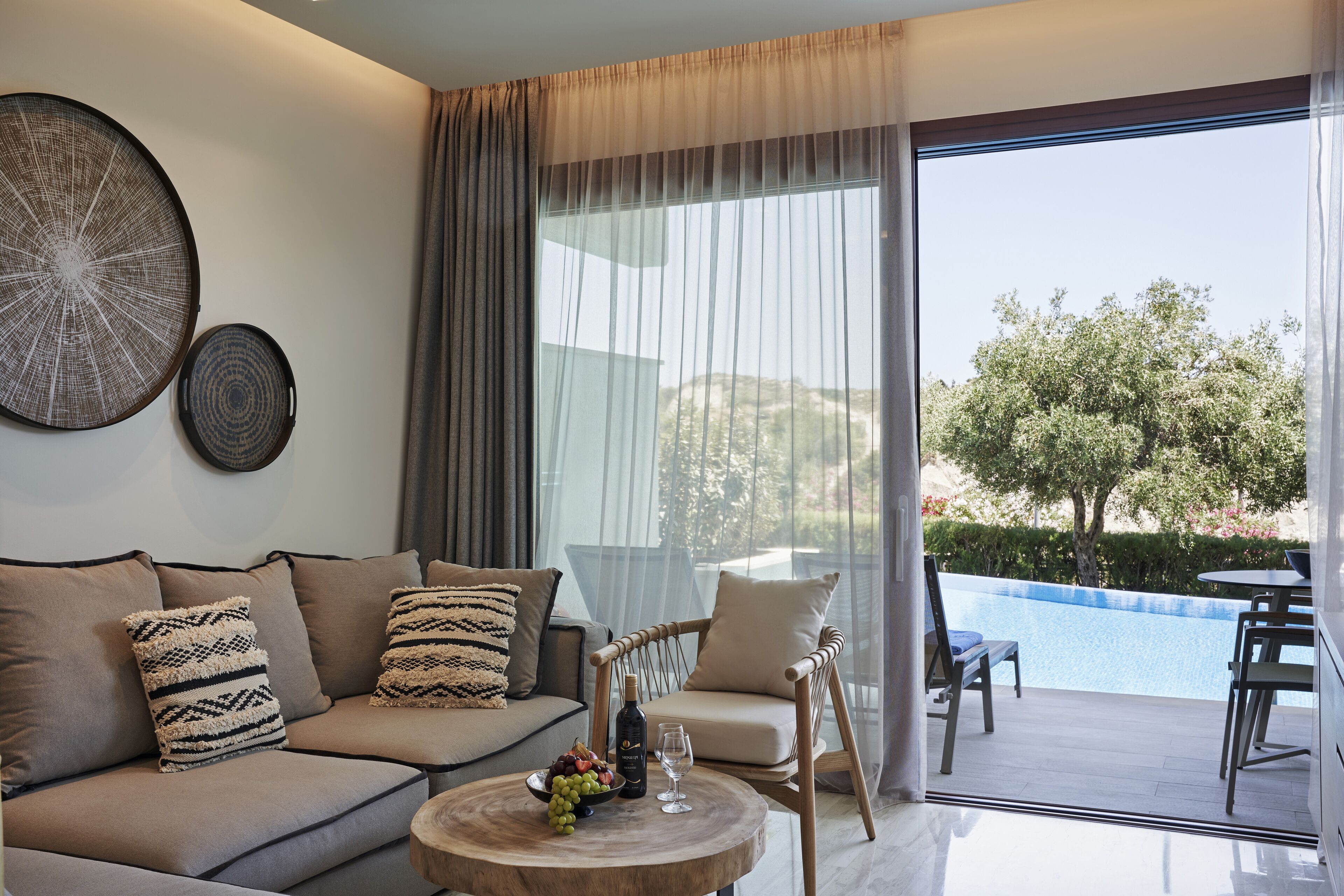 A modern living room with a sofa, a dining table, and a view of a swimming pool.