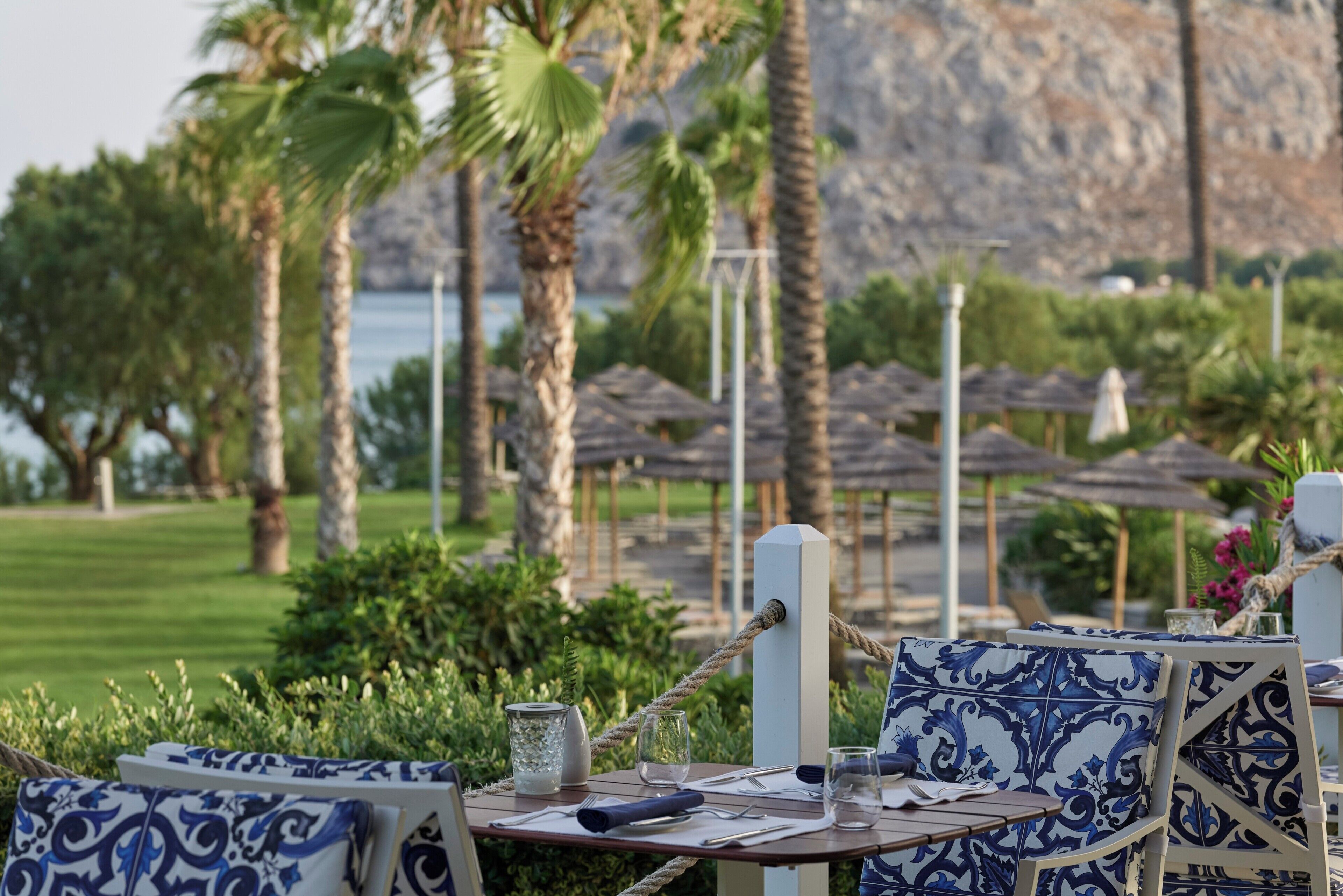 Une table dressée en plein air, offrant une vue sur un paysage montagneux, entourée de palmiers et de parasols.