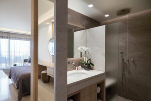 Un baño moderno con un espejo grande, un lavabo, una ducha y una orquídea en maceta.