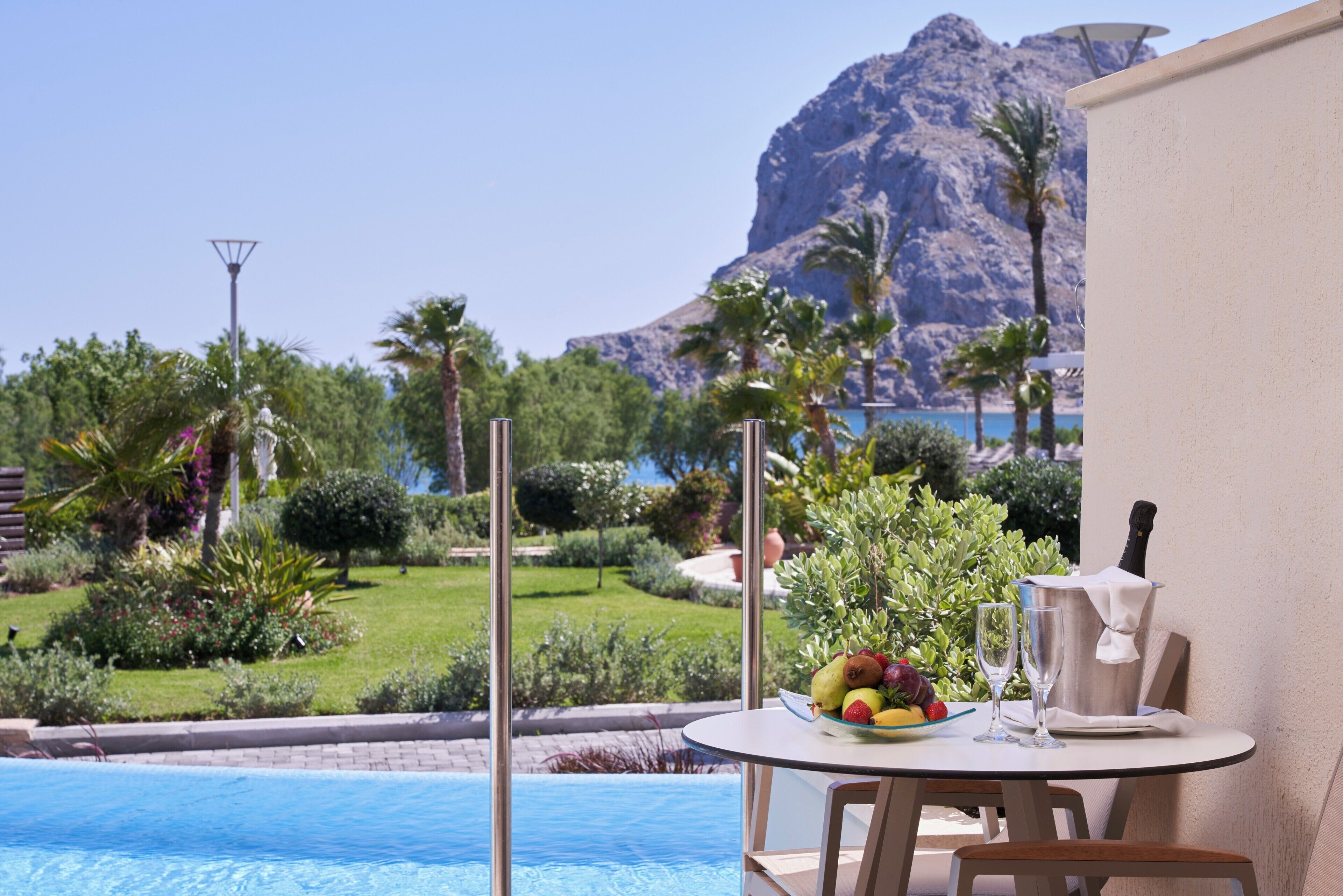 Ein Tisch am Pool mit Obst, einem Messer und einem Glas, mit Blick auf einen Pool vor einer Bergkulisse.