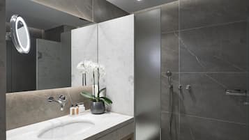 A modern bathroom with a marble sink, a mirror, a potted orchid, and a shower area.