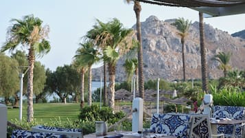 Espace extérieur aménagé avec des coussins à motifs, une table dressée avec des couverts, et une vue sur un paysage montagneux.