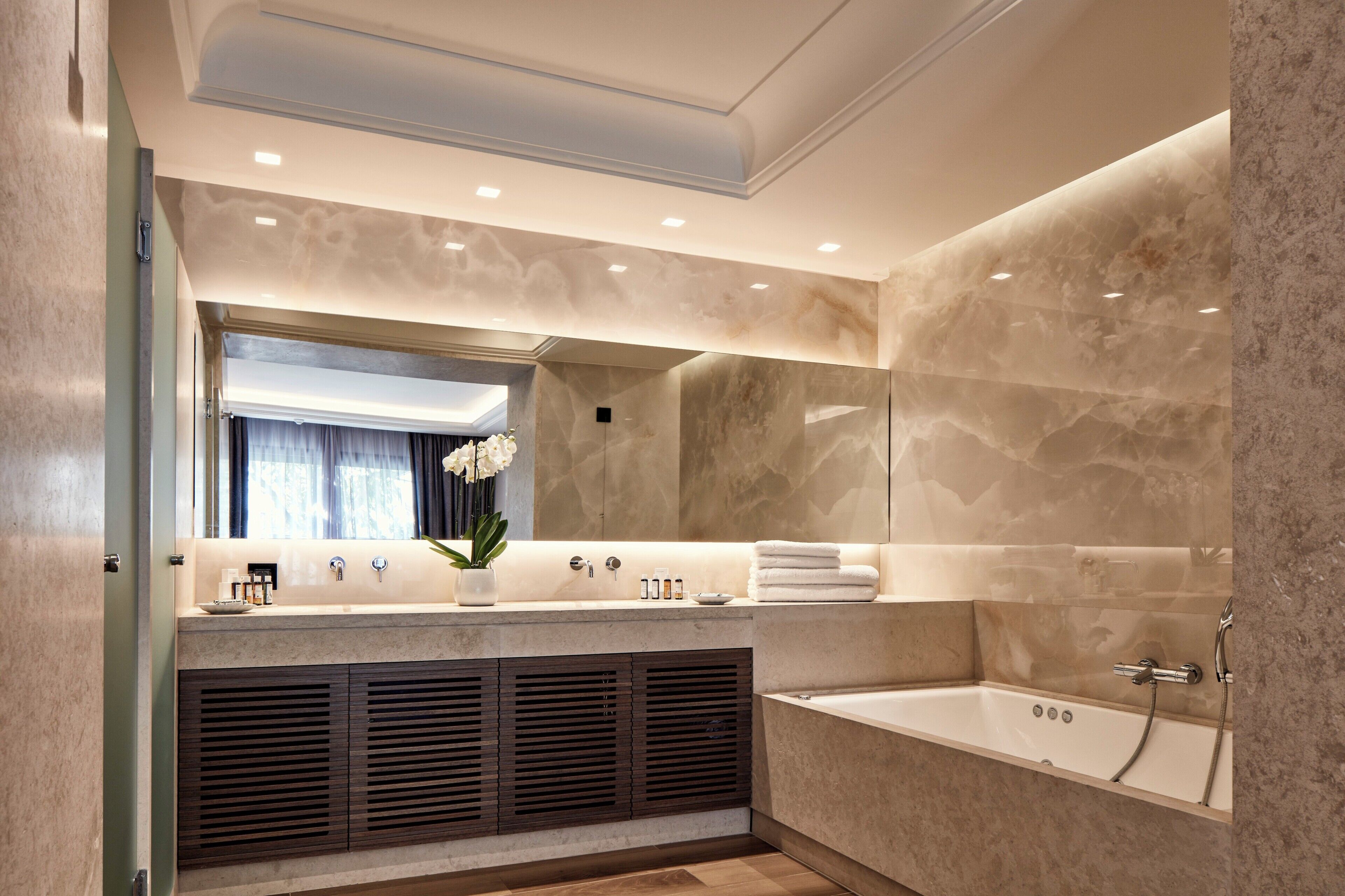 A modern bathroom with a large mirror, a bathtub, and a vanity with a sink and towel rack.
