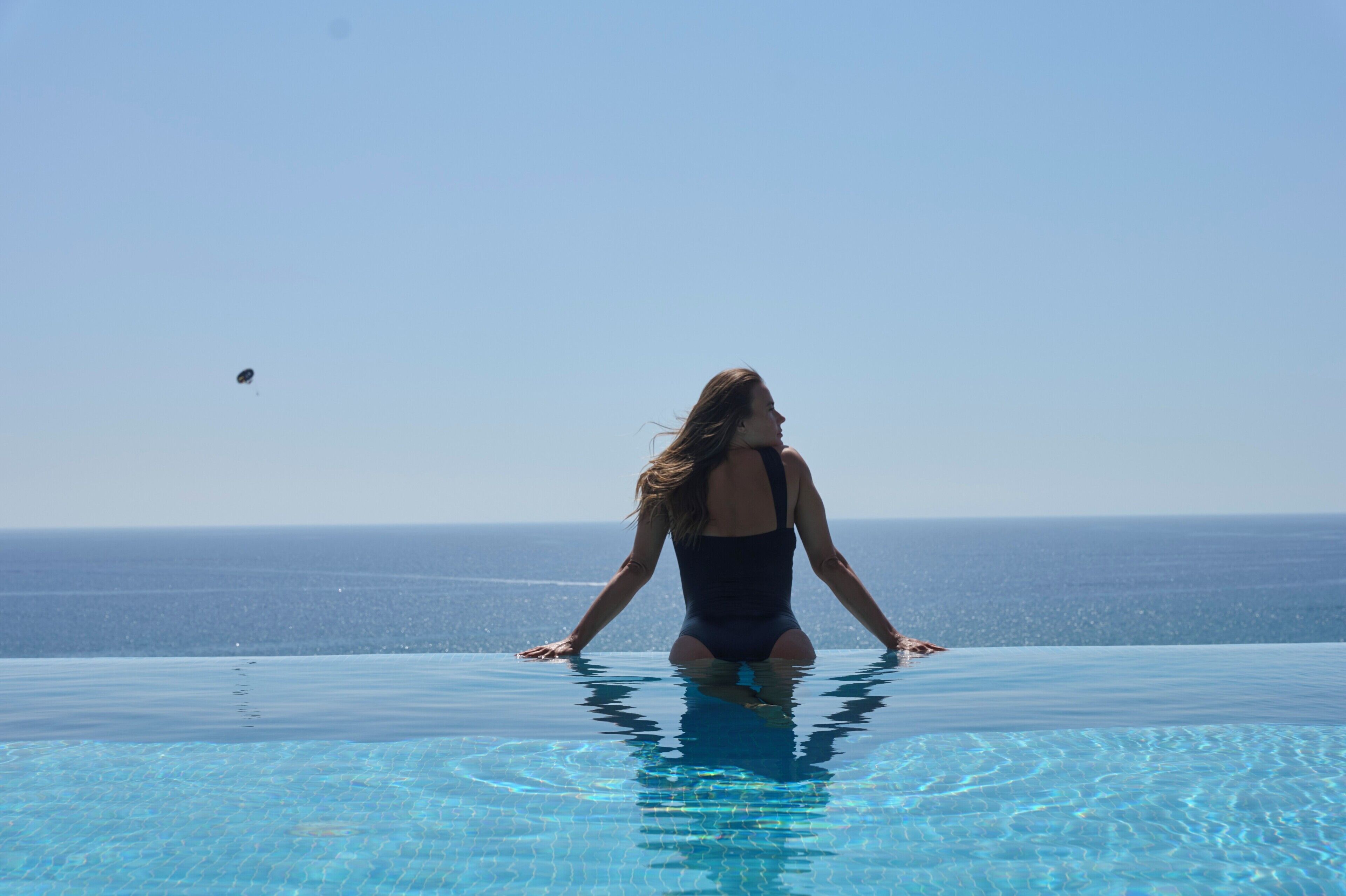 A person in a swimsuit at the edge of a pool with a view of the ocean.