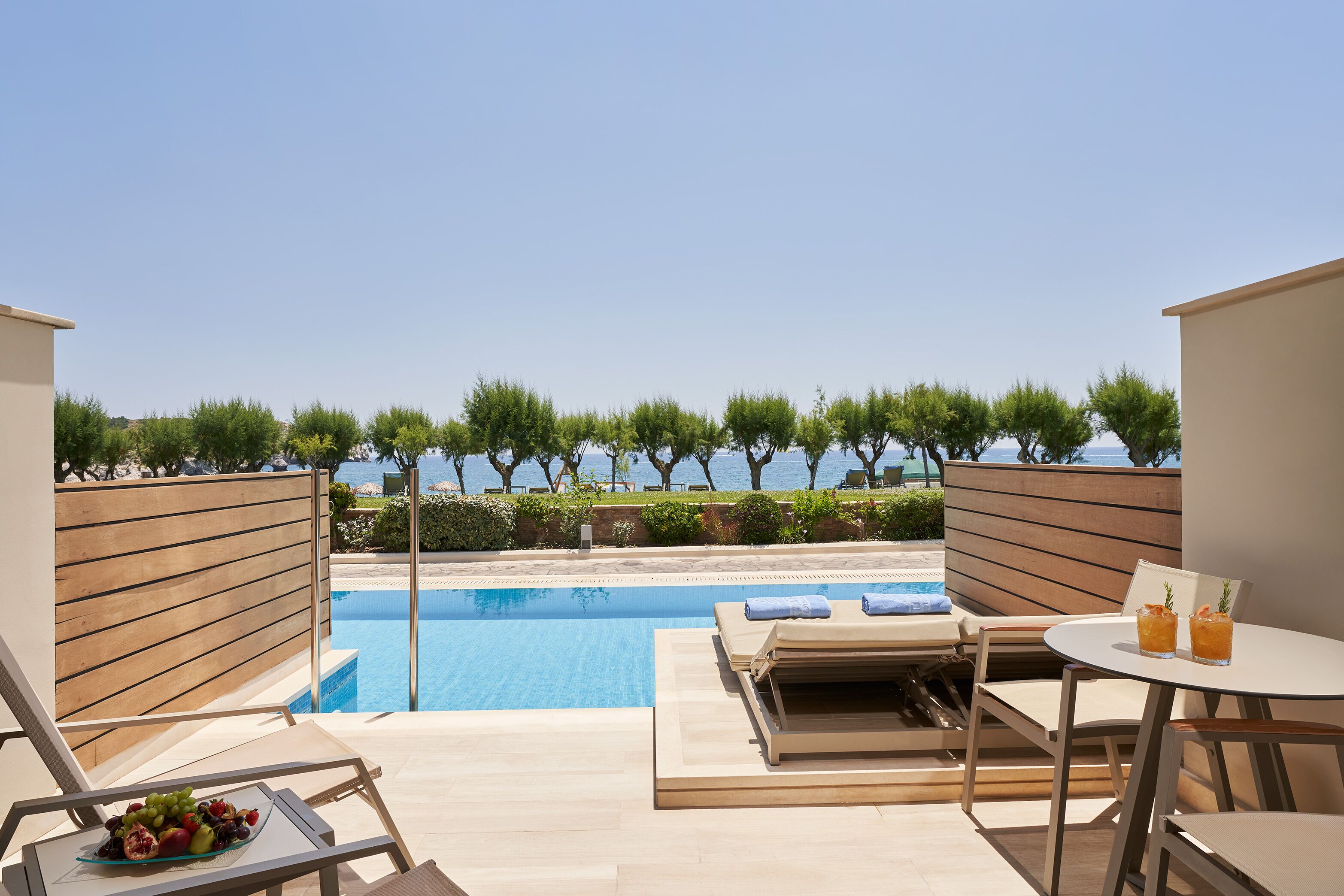 A poolside area with lounge chairs, a table with drinks, and a view of the sea.