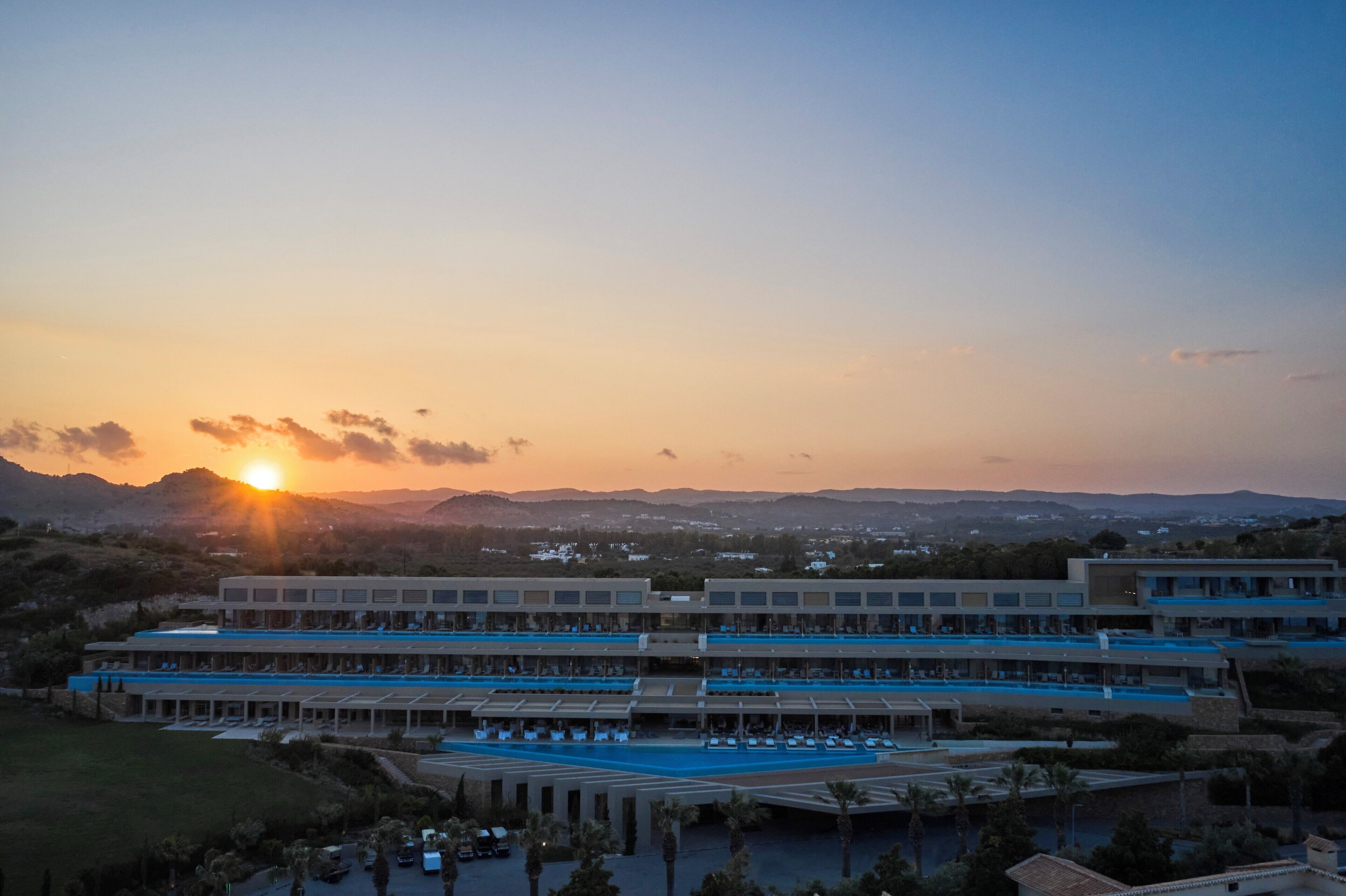 A hotel with multiple floors, a swimming pool, and a view of the surrounding landscape.