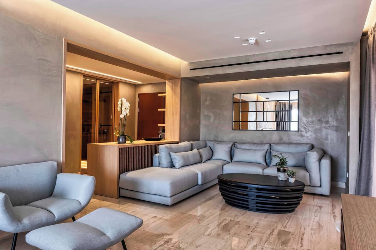 A modern living room with a sofa, armchairs, a coffee table, and a reception area with a counter and plants.