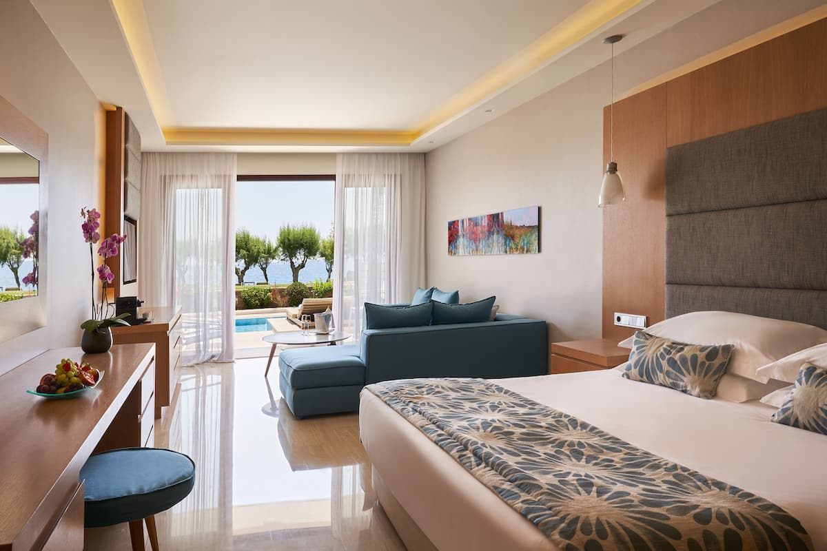 A modern hotel room with a large bed, a desk, and a view of the sea.