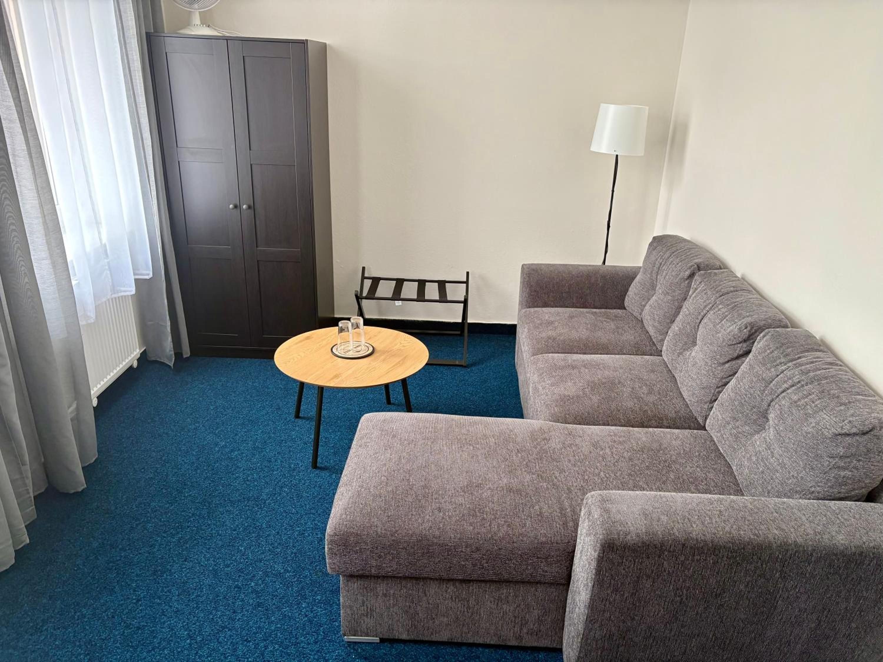 Un salon avec un canapé gris, une petite table ronde sur laquelle reposent deux verres, un lampadaire et une armoire en bois foncé.