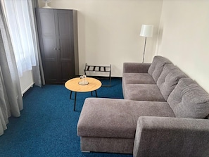 A living room with a grey sofa, a small round table with two glasses, a floor lamp, and a dark wooden wardrobe.