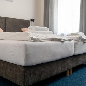 A neatly made bed with white linens, a grey upholstered headboard, and a blue carpeted floor. - CB Royal (CESKE BUDEJOVICE)