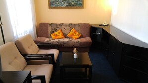 A hotel room with a sofa, two armchairs, a coffee table, a small table with a vase, a painting on the wall, and a telephone on a side table.