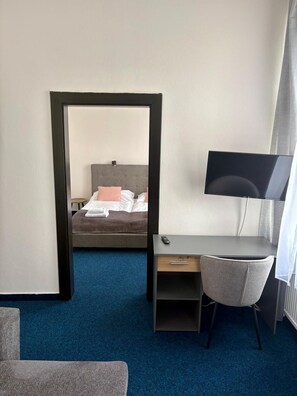 A hotel room with a bed, a desk with a chair, a television, and a mirror.